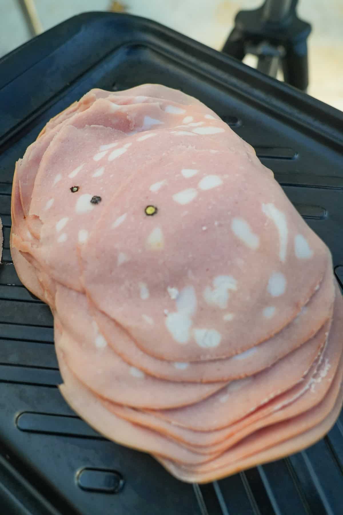 A stack of mortadella slices on top of a cast iron pan