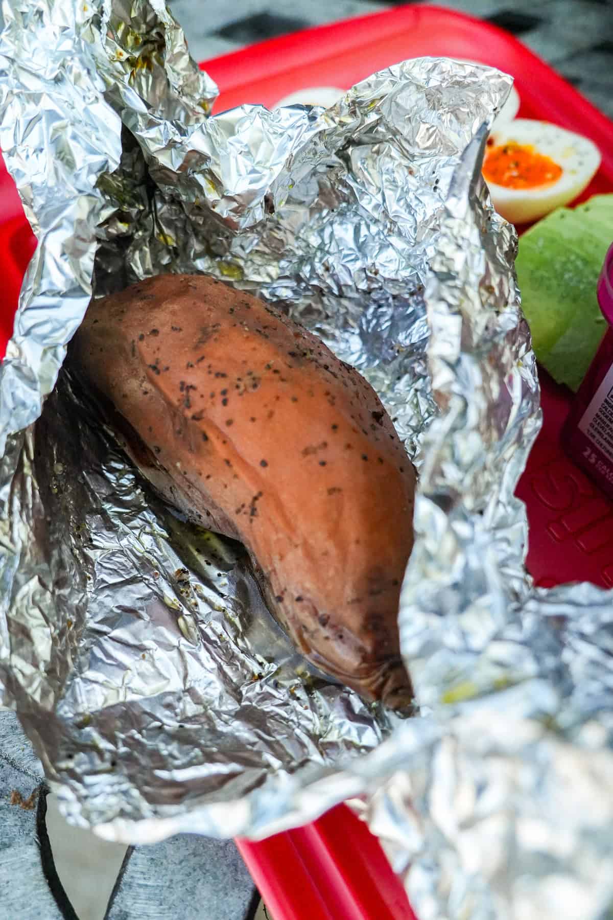 A whole sweet potato wrapped in aluminum foil for baking