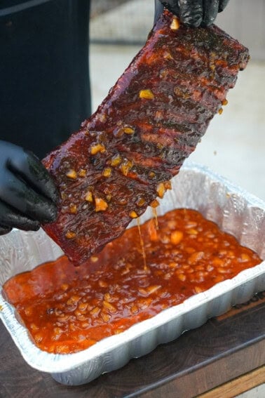 Derek Wolf holding up a rack of bourbon peach ribs after they've been dipped in the glaze