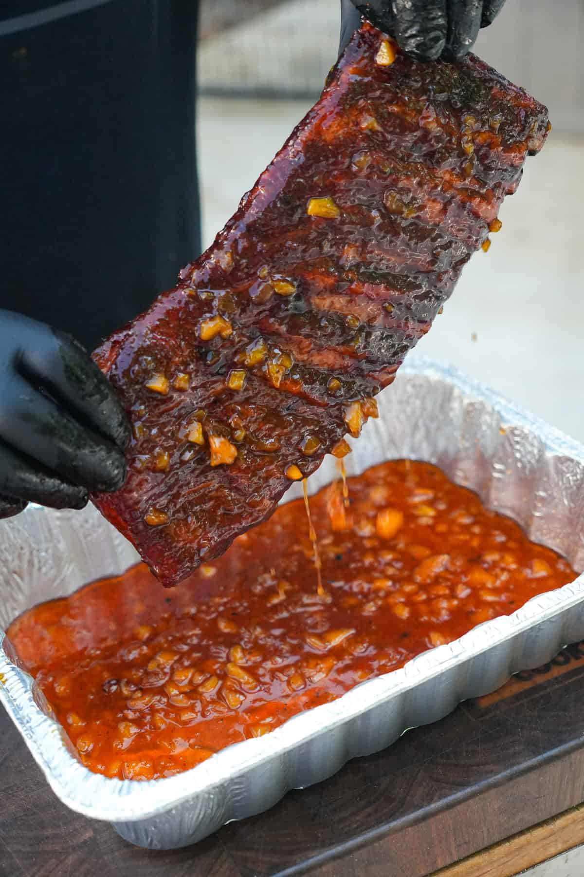 Derek Wolf holding up a rack of bourbon peach ribs after they've been dipped in the glaze