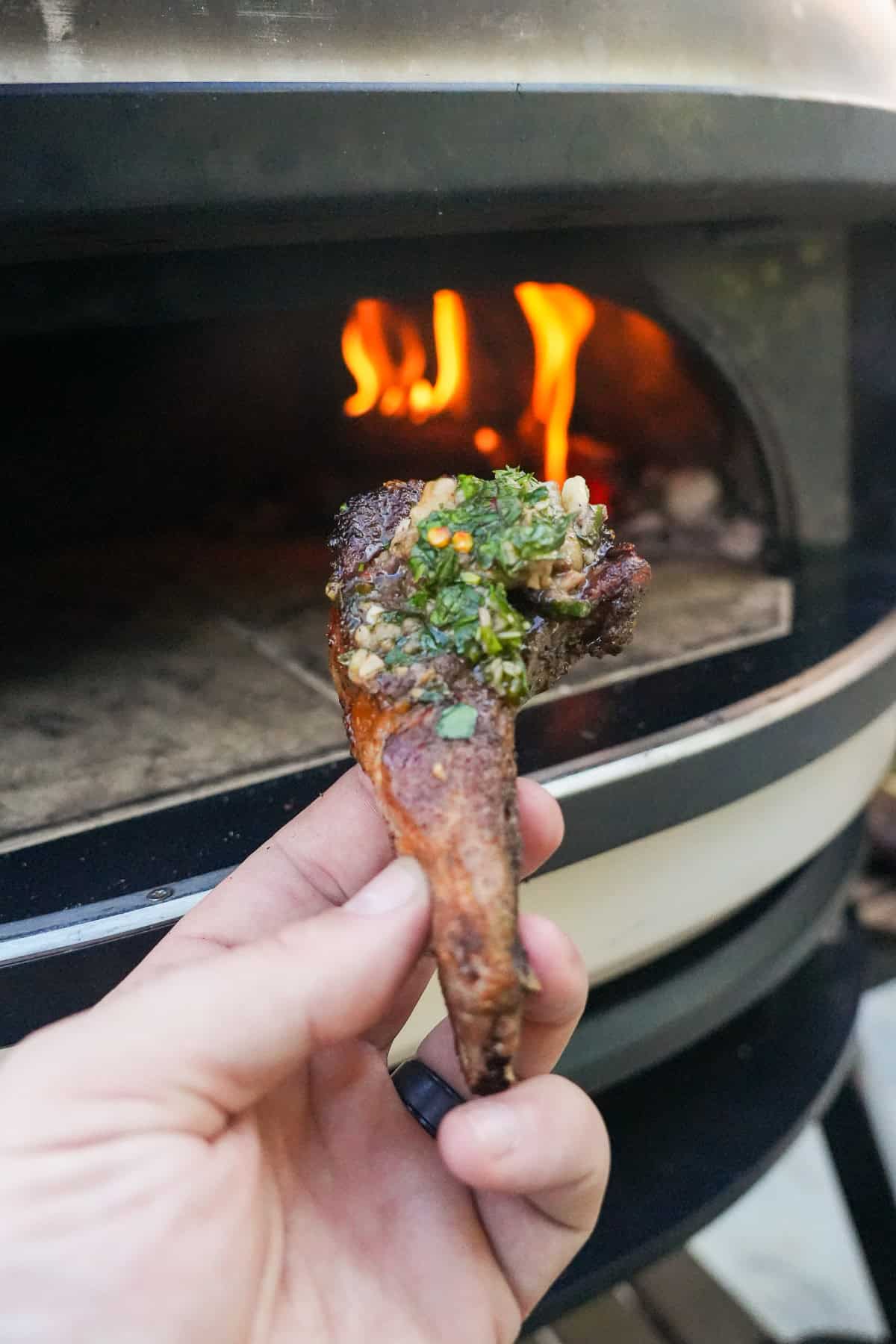 Derek Wolf holding up a lamb chop with bone marrow smeared on it and topped with mint chimichurri