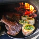A cast iron skillet with lamb chops, bone marrow rounds filled with mint chimichurri in a pizza oven, with a live fire in the background