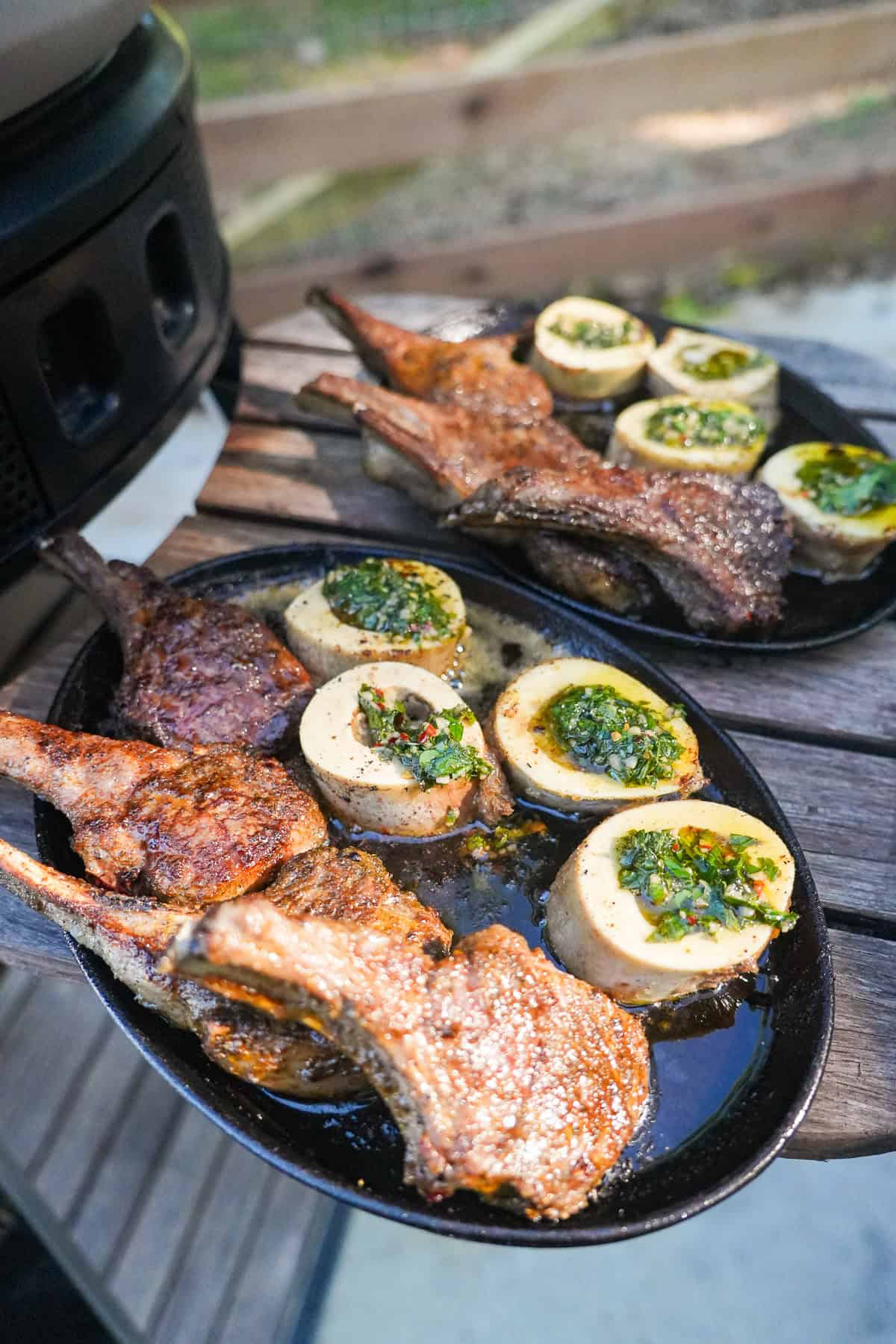 Two plates of cooked lamb chops from the pizza oven and bone marrow rounds filled with mint chimichurri