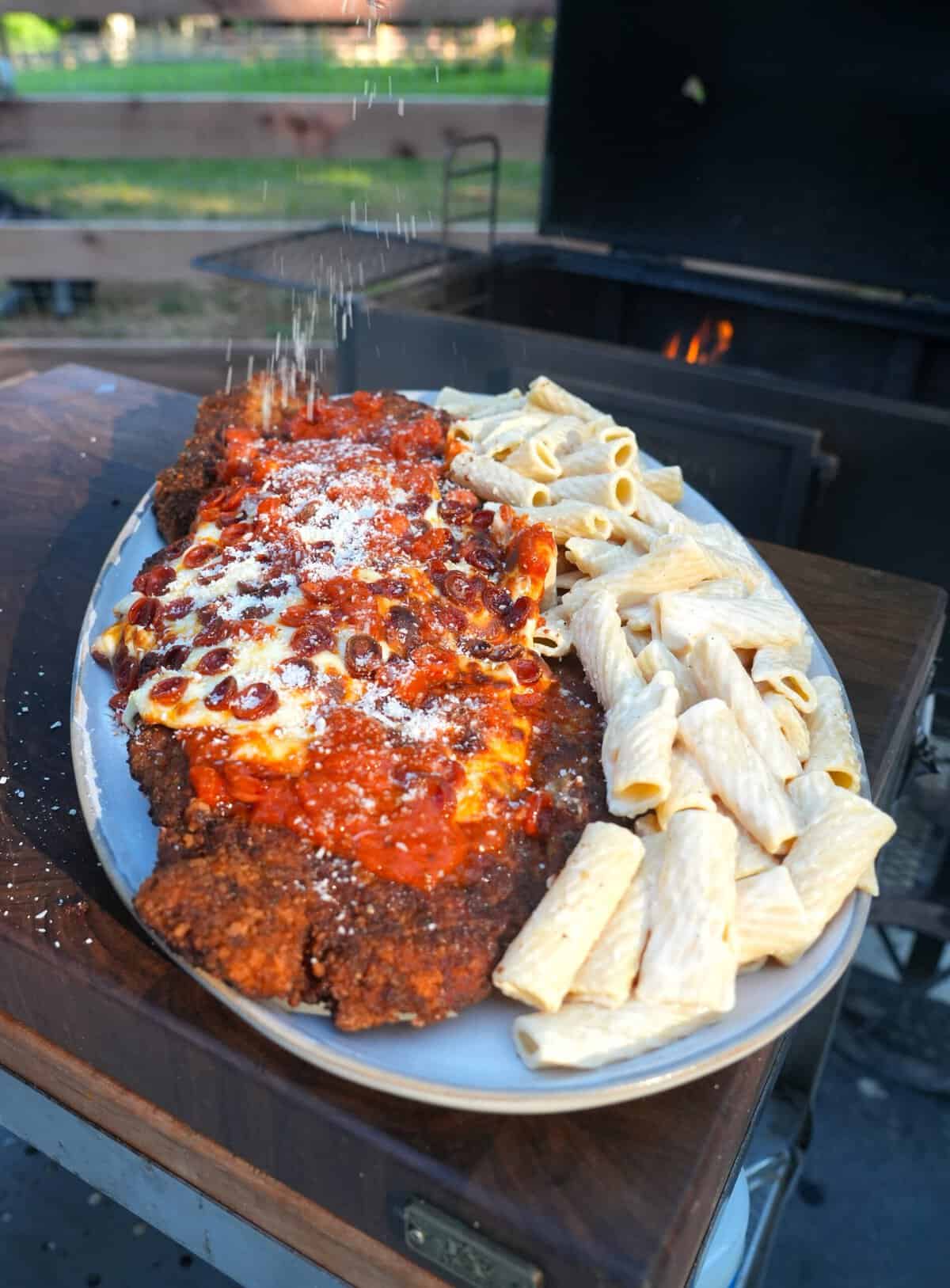 Adding extra grated Parmesan cheese to the finished chicken pizza Parmesan dish, with pasta on the side