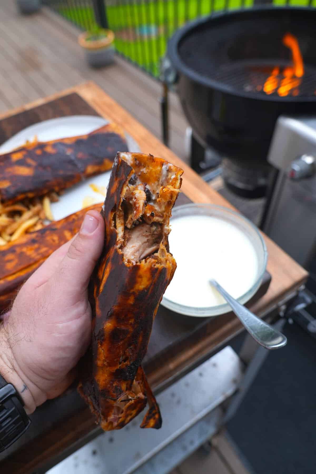Derek Wolf holding up a crispy chicken shawarma sandwich with a bite taken out of it and toum sauce in a bowl in the background
