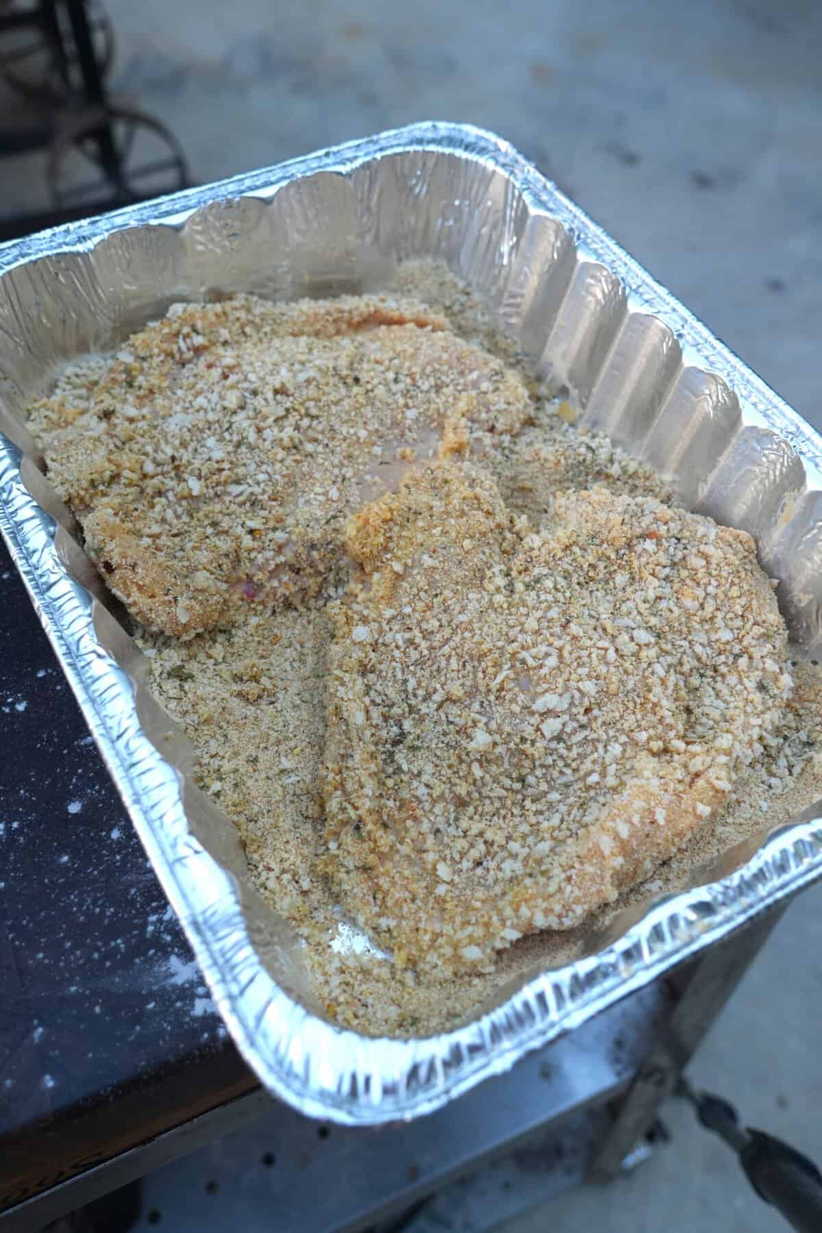 Dredging chicken cutlets in Italian breadcrumbs, in an aluminum roasting pan