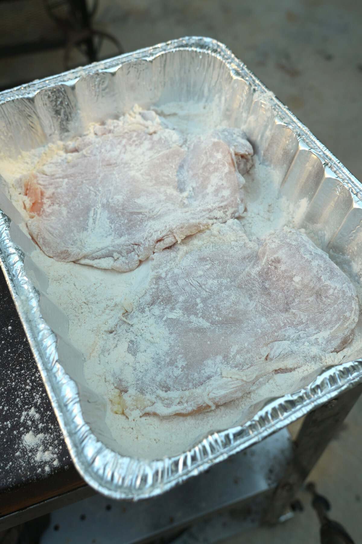 Dredging chicken cutlets in flour in an aluminum roasting pan
