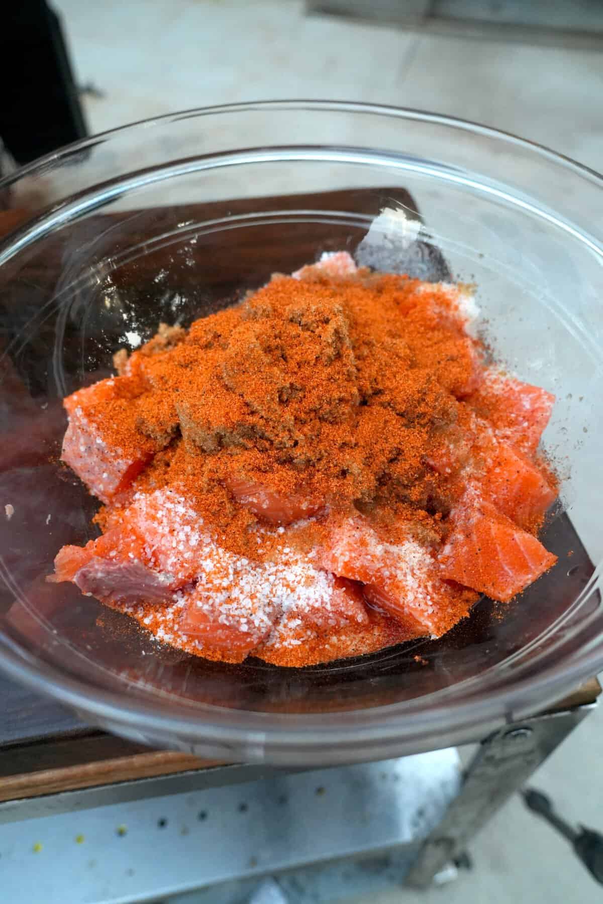 Seasoning cubes of salmon in a glass bowl with a maple bourbon cure