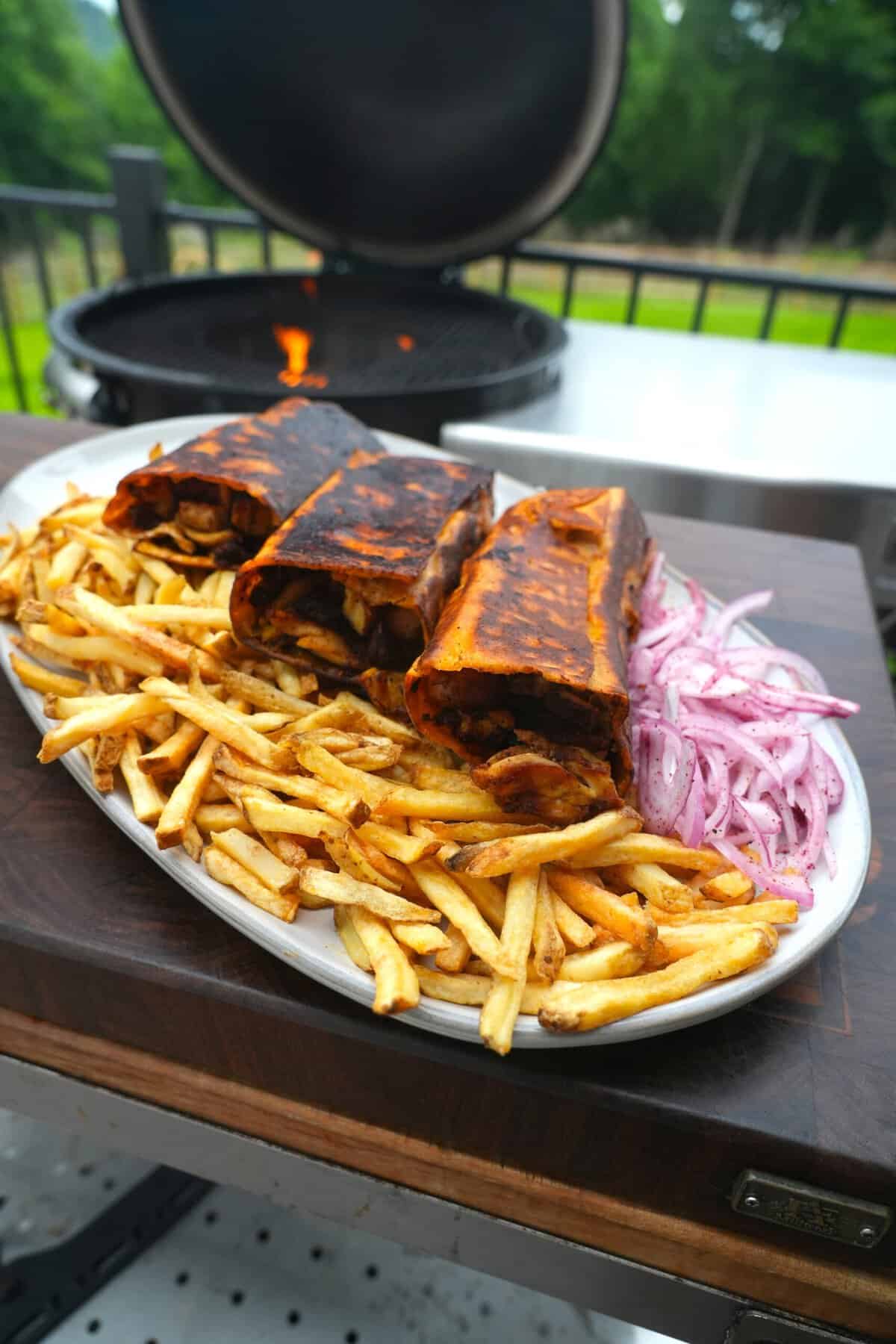 Finished chicken shawarma on a platter with fries and sliced pickled red onions