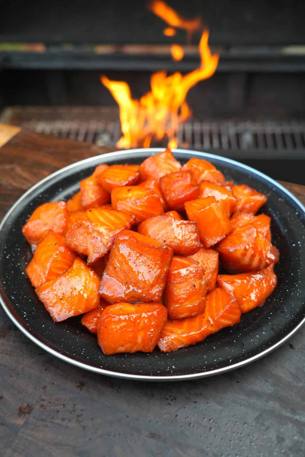 A finished plate of maple bourbon salmon burnt ends, with a grill fire in the background
