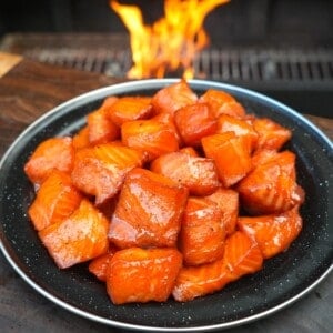 A finished plate of maple bourbon salmon burnt ends, with a grill fire in the background