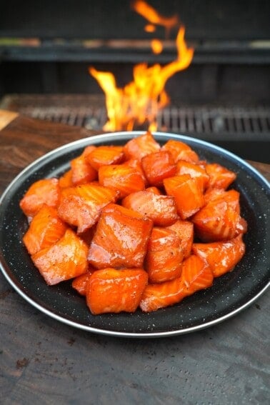 A finished plate of maple bourbon salmon burnt ends, with a grill fire in the background