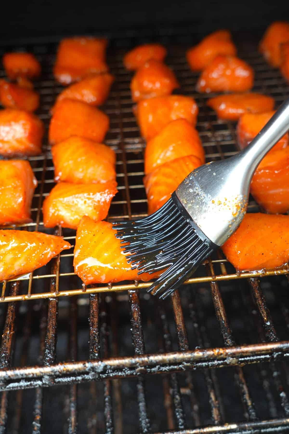 Brushing salmon cubes with maple bourbon glaze on the smoker, using a grill brush