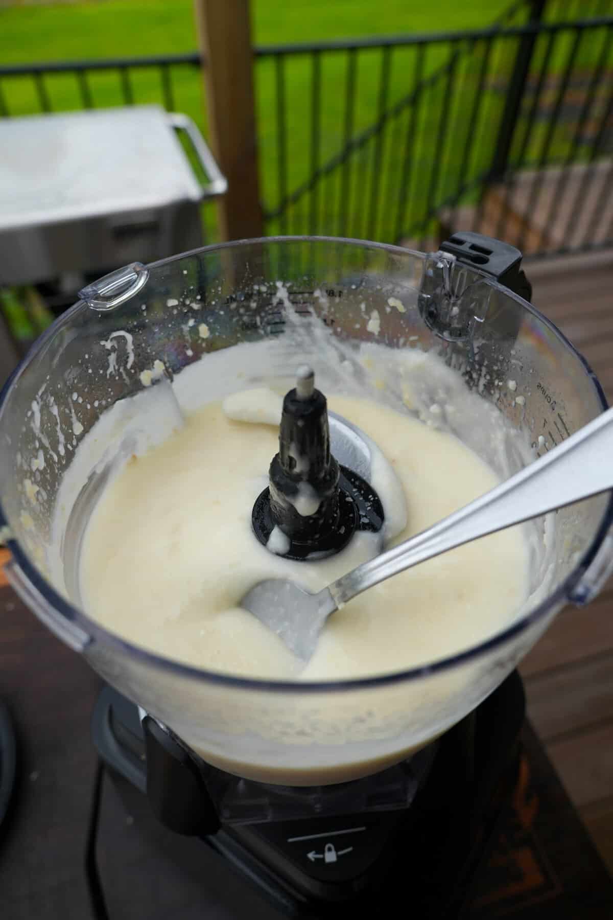 Homemade toum sauce in a food processor with a spoon