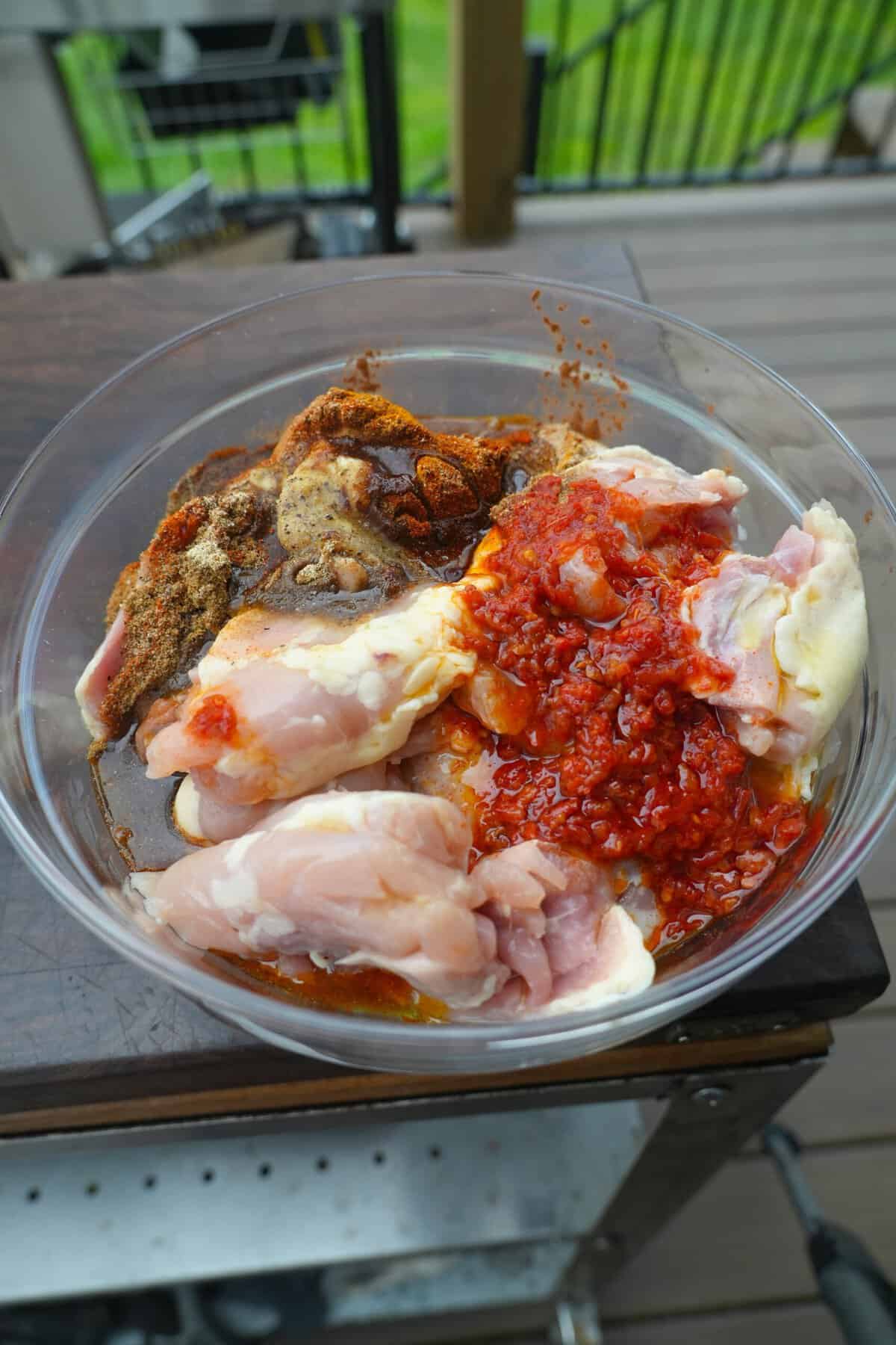 Boneless chicken thighs in a bowl with a collection of spices for marinating
