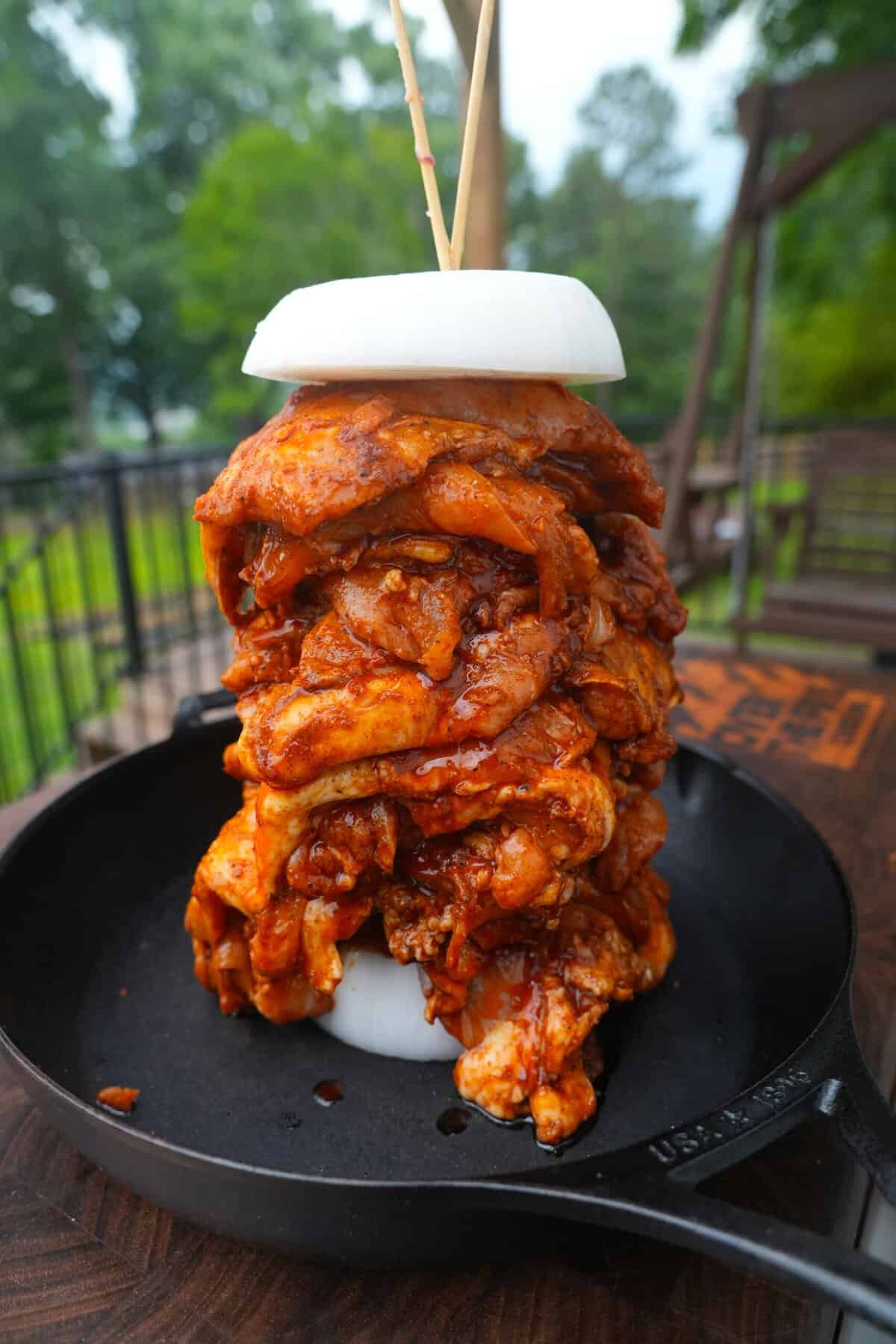 Marinated chicken thighs stacked on a vertical spit with white onions stacked on either side