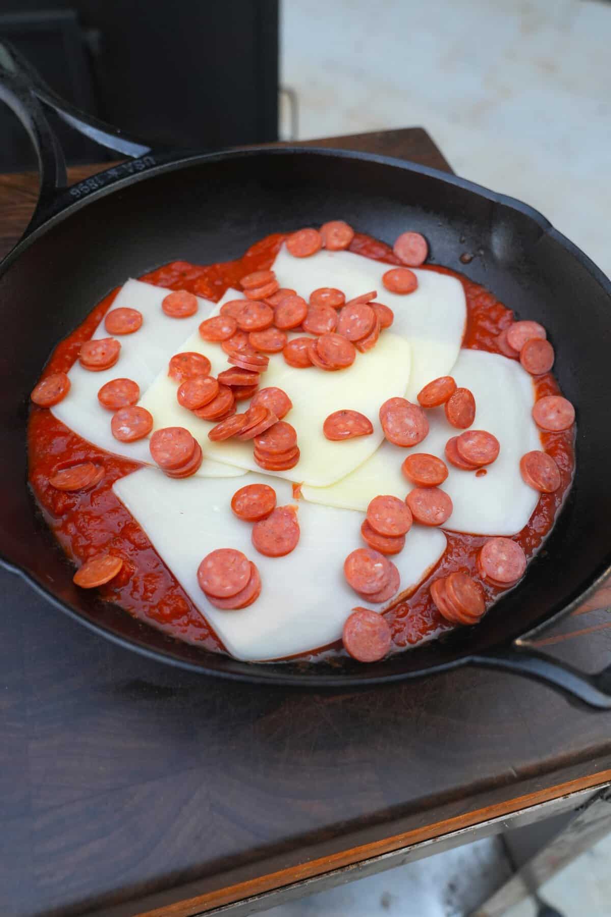 Uncooked mozzarella cheese, pepperoni and marinara sauce in a cast iron skillet