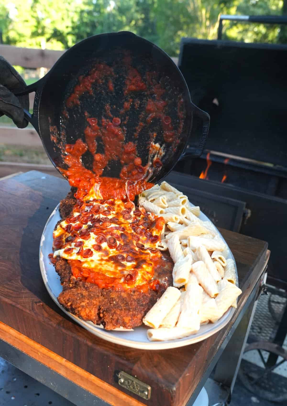 Pouring pizza sauce and cheese over the finished chicken Parmesan, with rigatoni Alfredo on the side