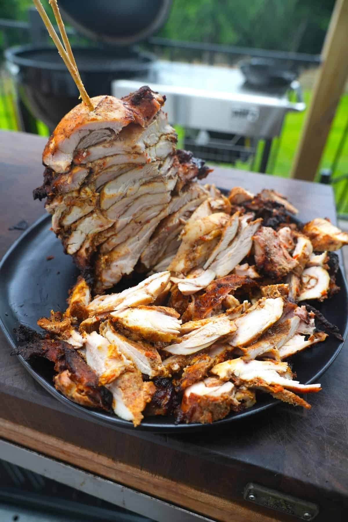 Slicing cooked boneless chicken thighs off the trompo and into the cast iron skillet