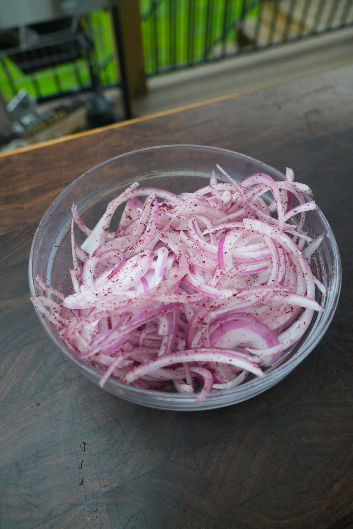 Sliced red onions with sumac powder and lemon juice in a small glass bowl