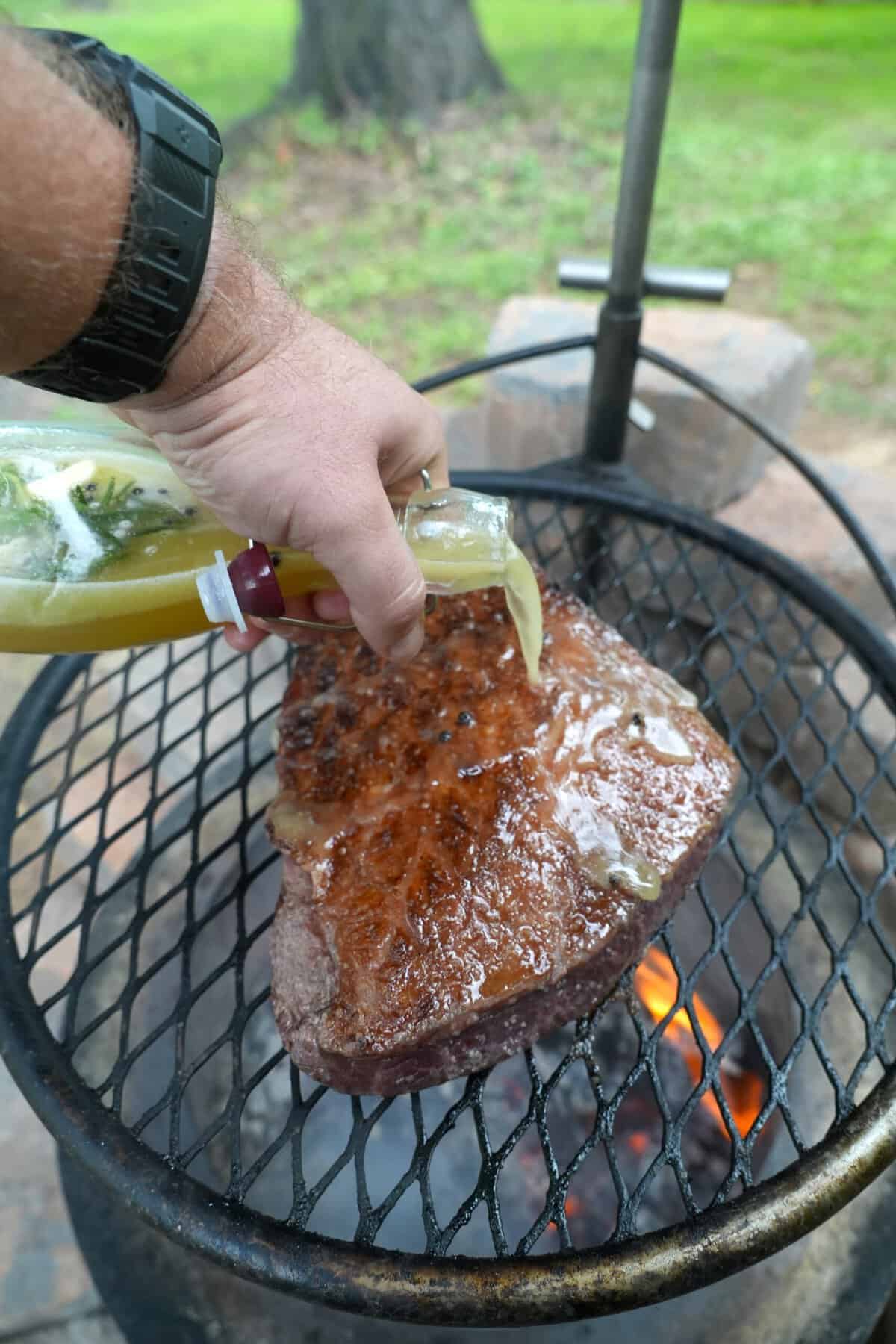 Derek Wolf using beer salmuera to baste a steak on a charcoal grill