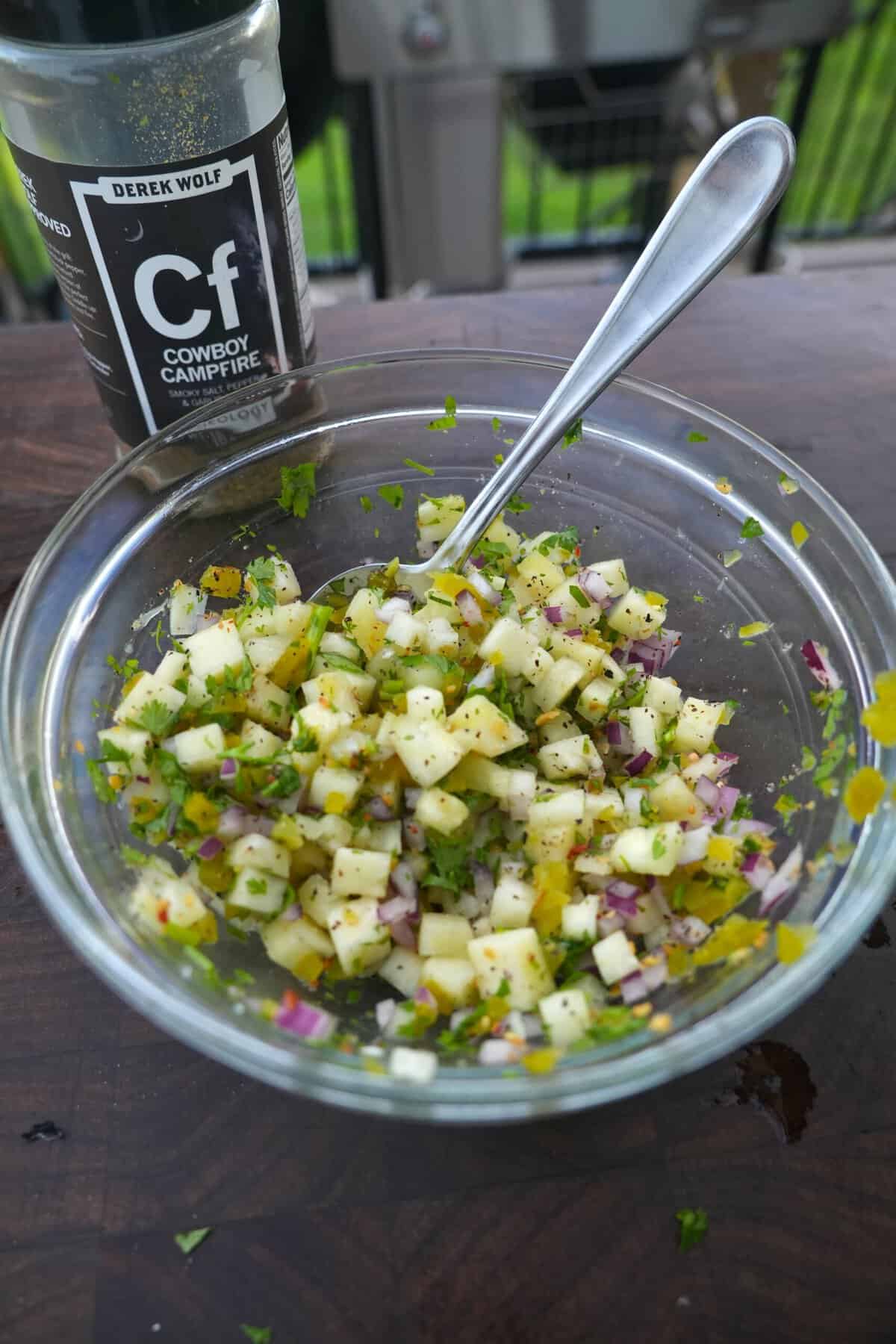 Mixing together ingredients for pineapple salsa in a small glass bowl, with Cowboy Campfire Rub in the background