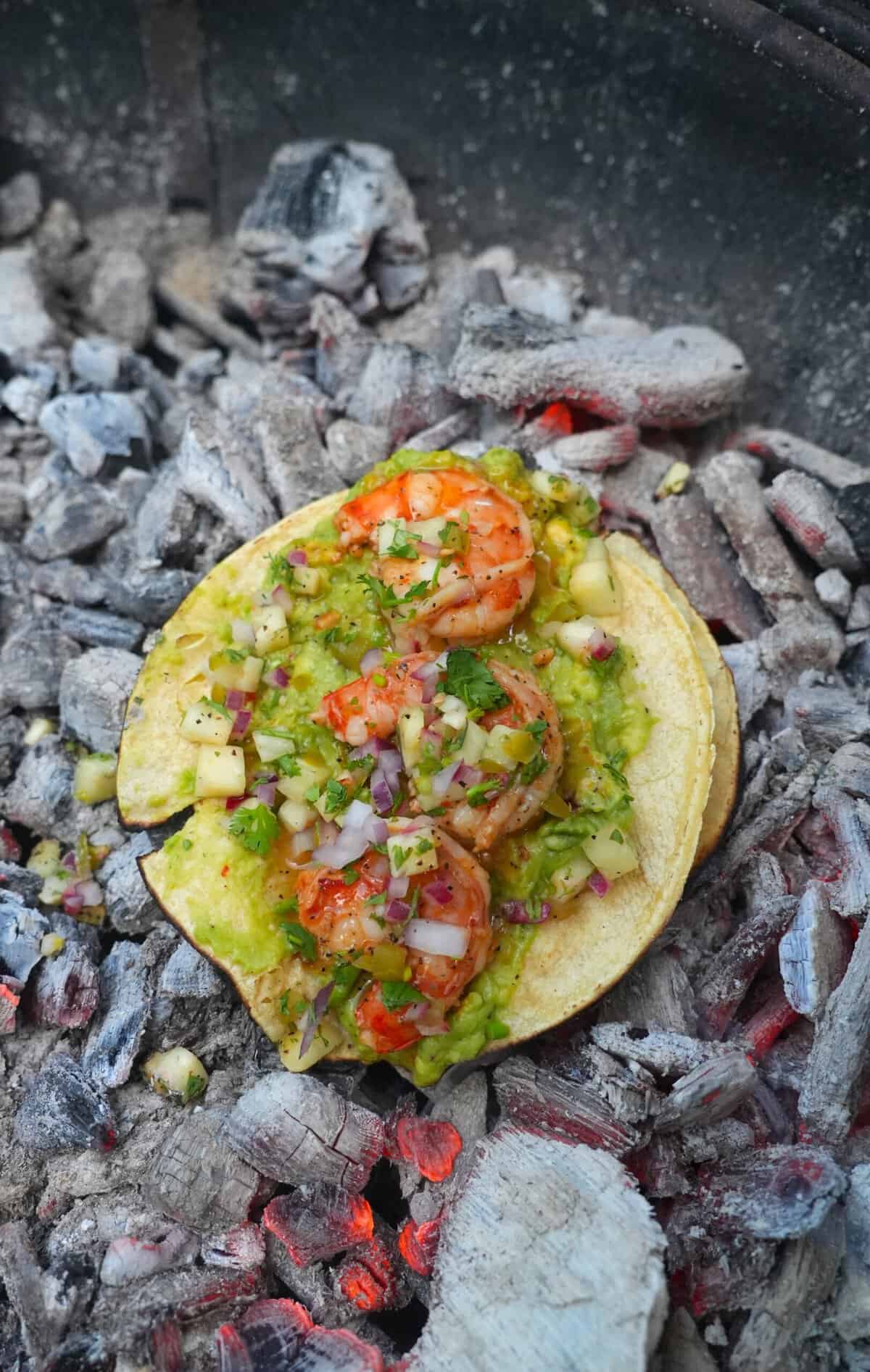 An assembled dirty shrimp taco with guacamole and pineapple salsa on top of hot coals