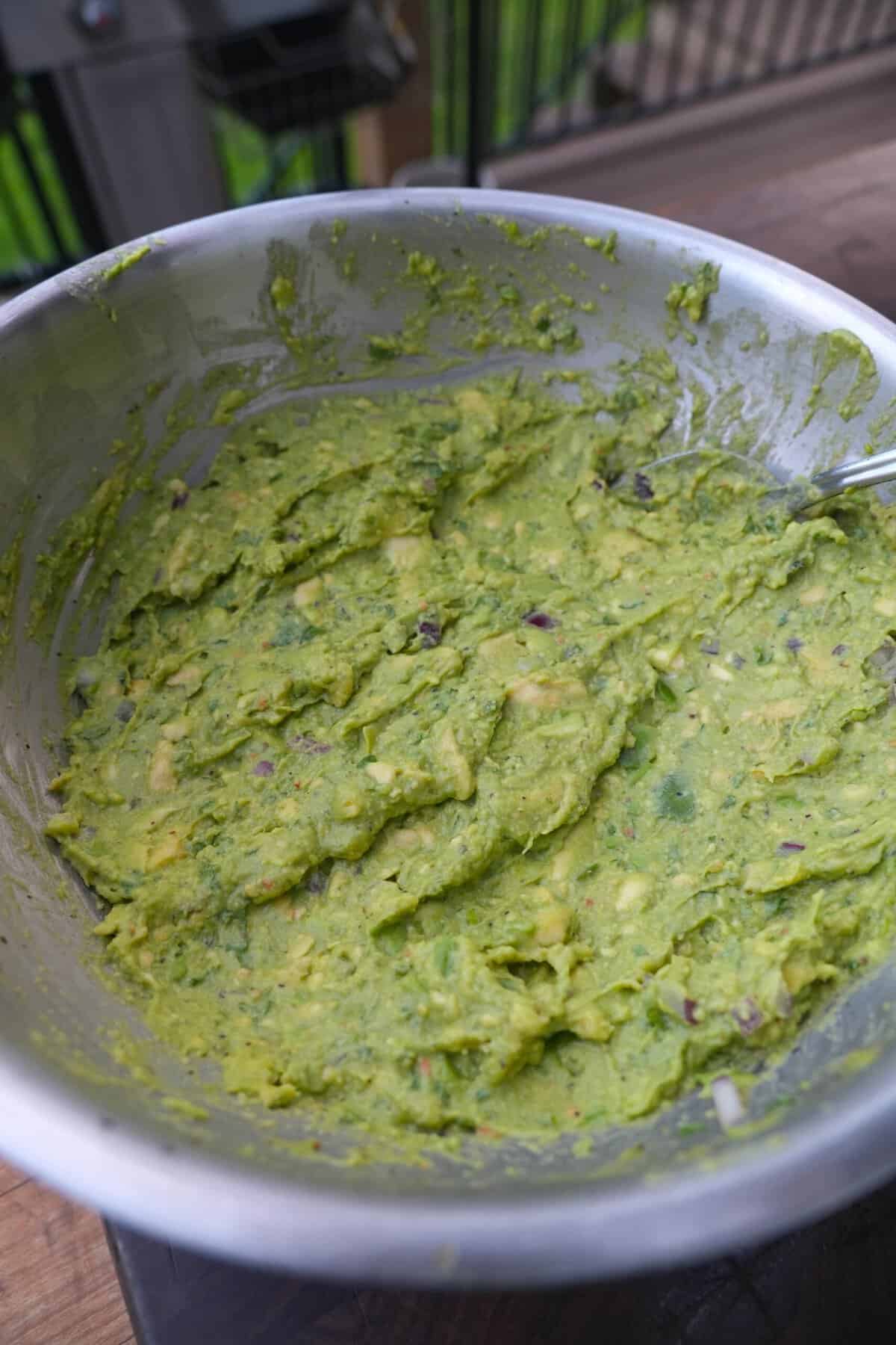 Mixing together avocado, red onion, lime juice and cilantro in a large bowl to make guacamole