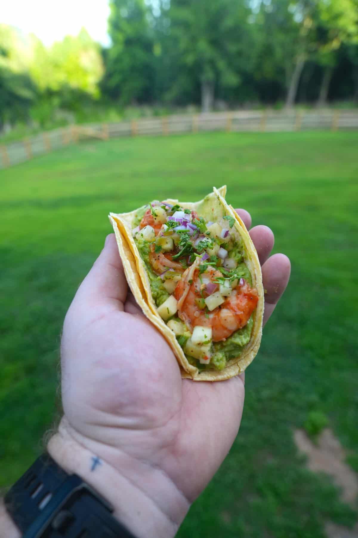 Derek Wolf holding up an assembled shrimp taco, before it goes onto the coals to become a dirty shrimp taco