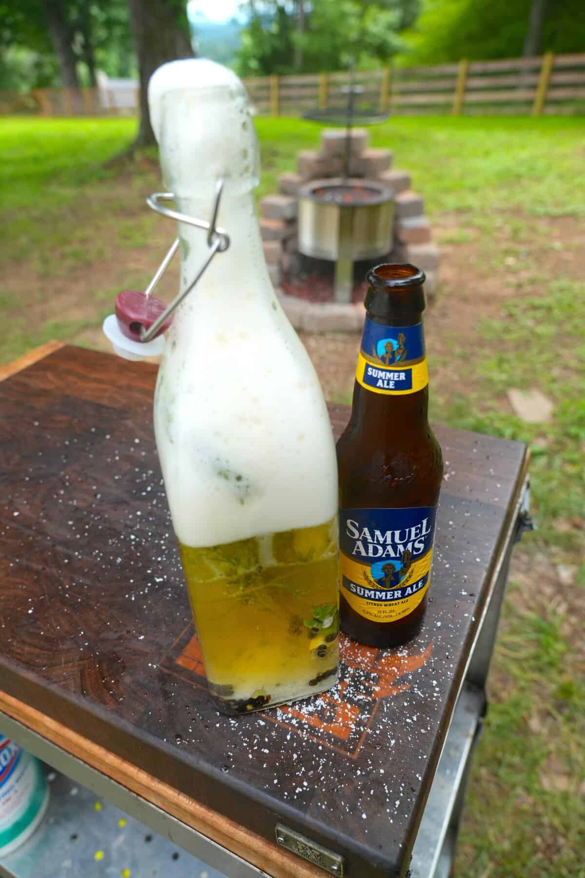 A clear glass bottle of beer salmuera, next to a bottle of Samuel Adams Summer Ale