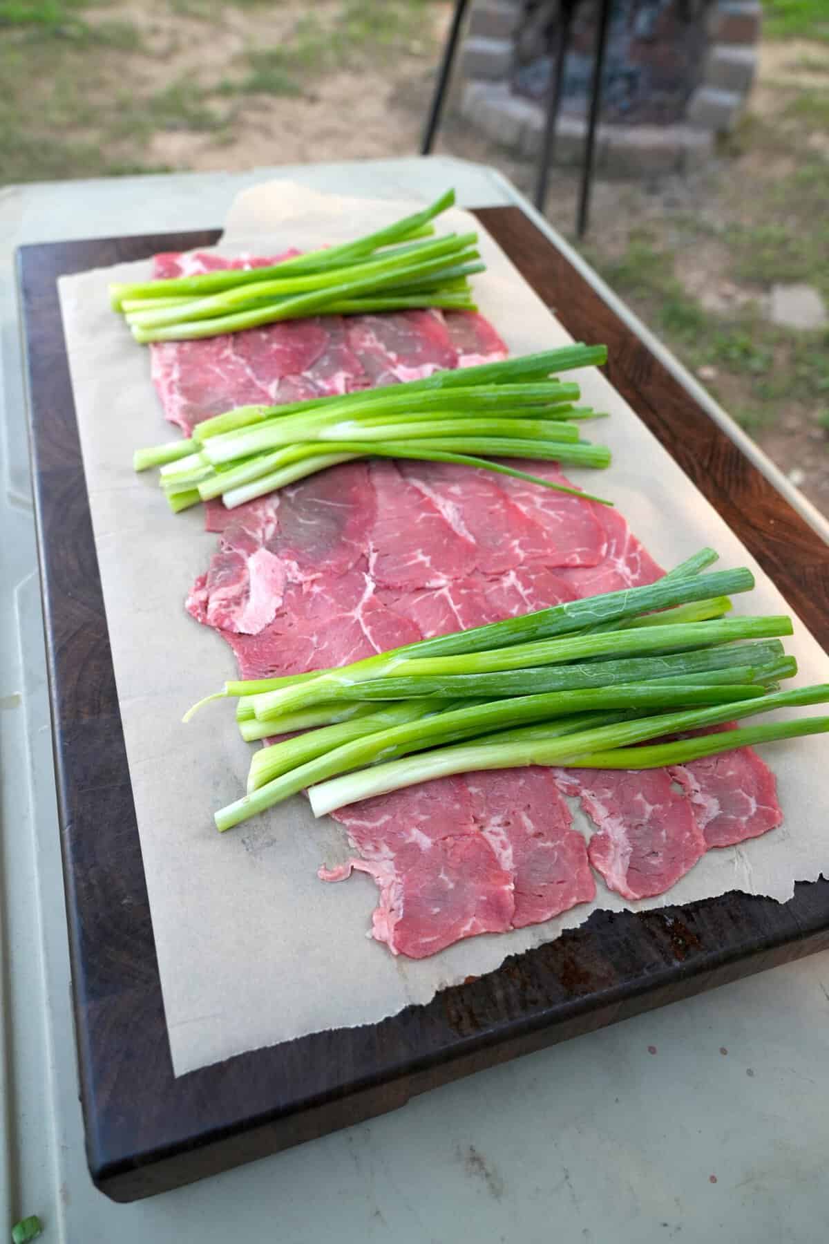 Adding bunches of scallions on top of beef and salmon for skewers