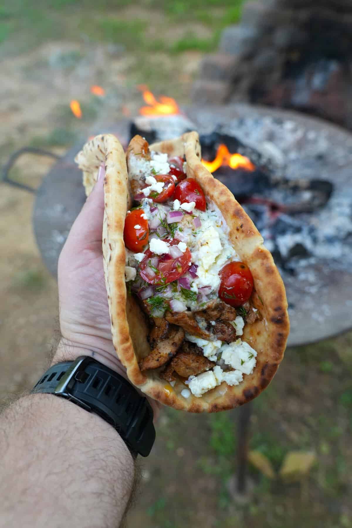 Derek Wolf holding a fully assembled chicken gyro in pita bread, with tomatoes and feta and tzatziki on top