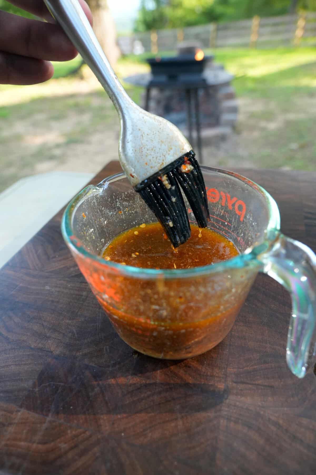 Using a grill brush to pick up butter baste from a glass measuring cup