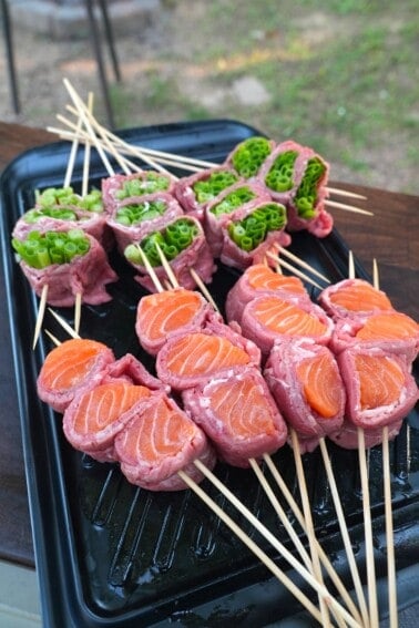 Assembled raw beef and salmon skewers on a cutting board, threaded on wood skewers
