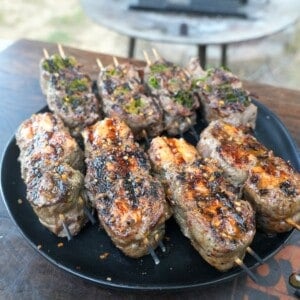 Grilled beef and salmon skewers on a plate with a grill fire in the background