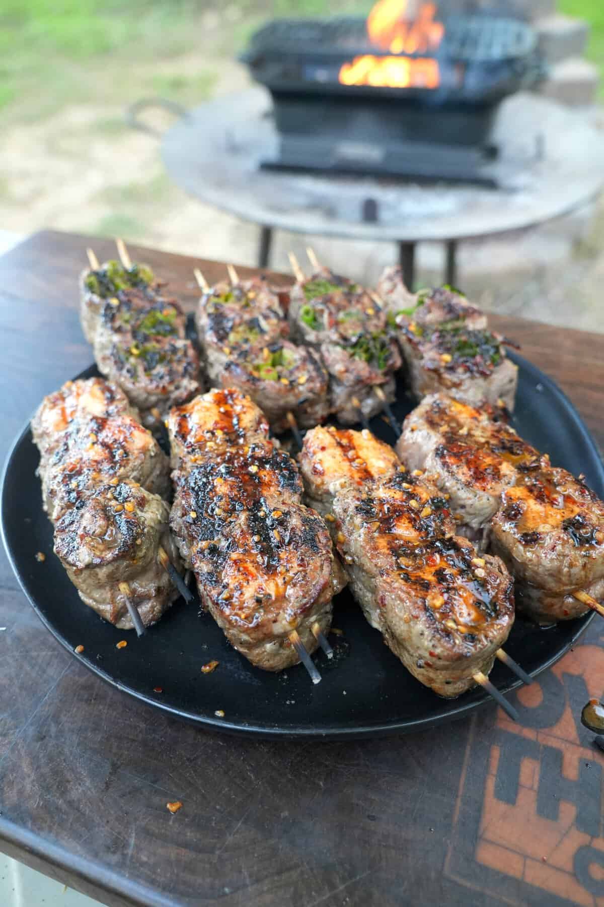 Grilled beef and salmon skewers on a plate with a grill fire in the background