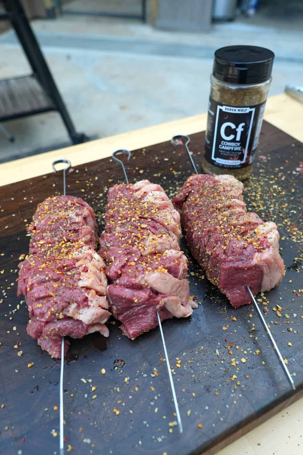 Raw picanha steak skewers seasoned with spices and ready for grilling.