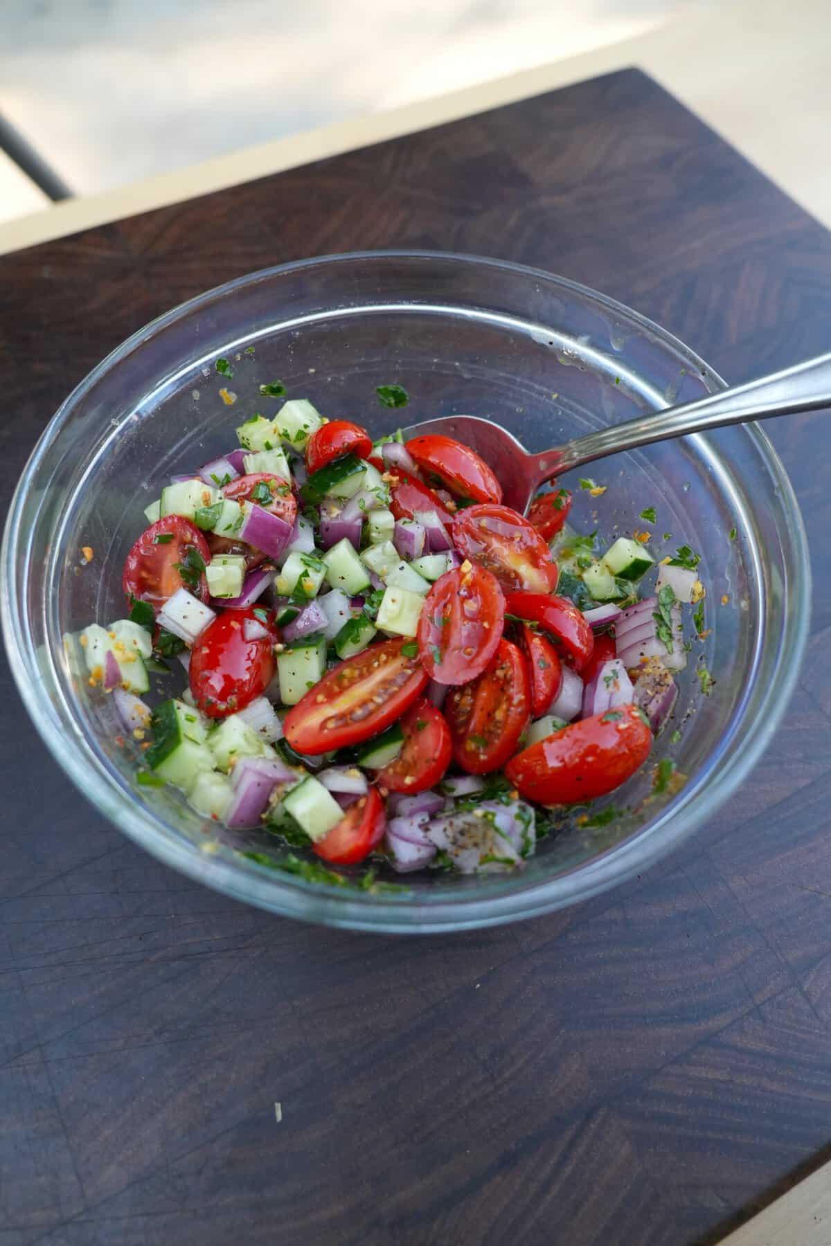 Colorful tomato and cucumber salad with red onion and herbs in a glass bowl.