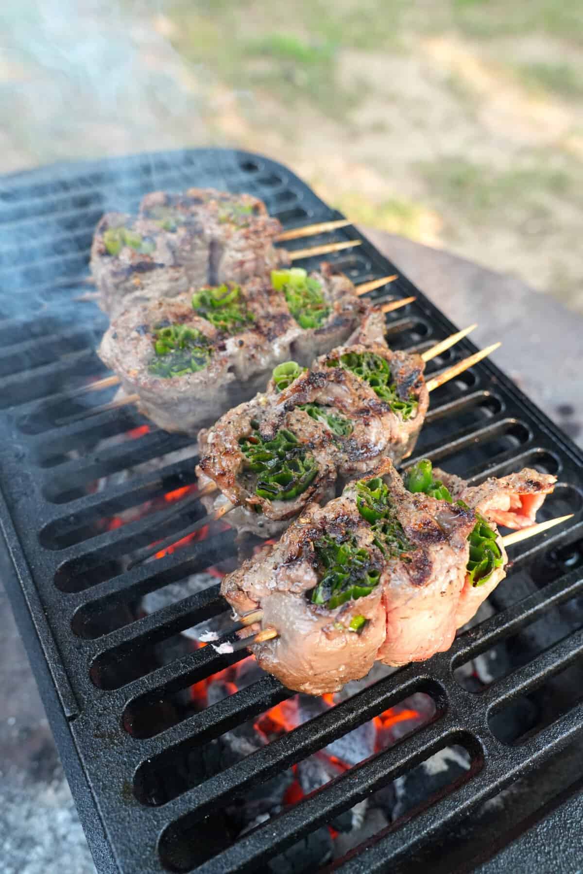 A side angle of beef and salmon skewers on the grill grates, using wooden skewers to hold them together