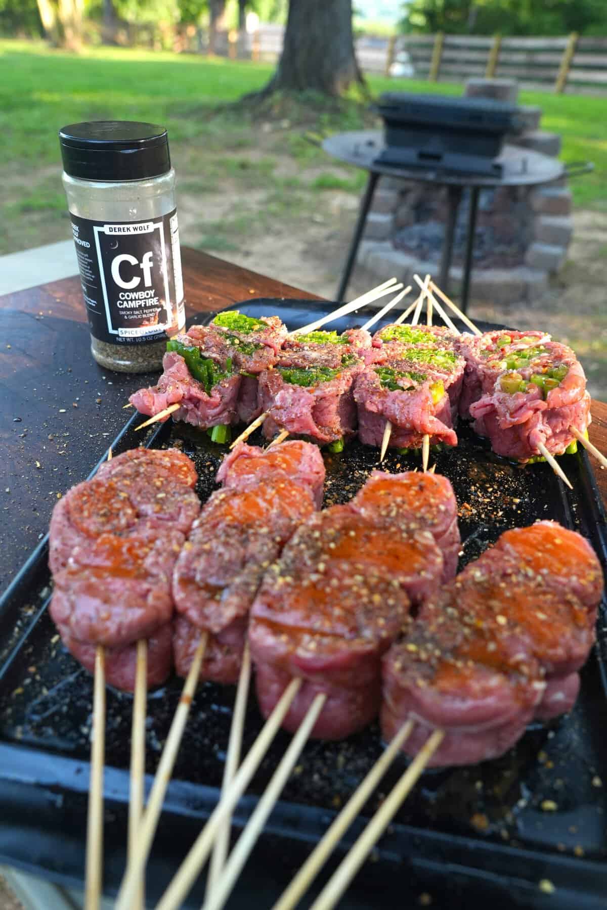 Seasoning the assembled beef and salmon skewers with a jar of Cowboy Campfire