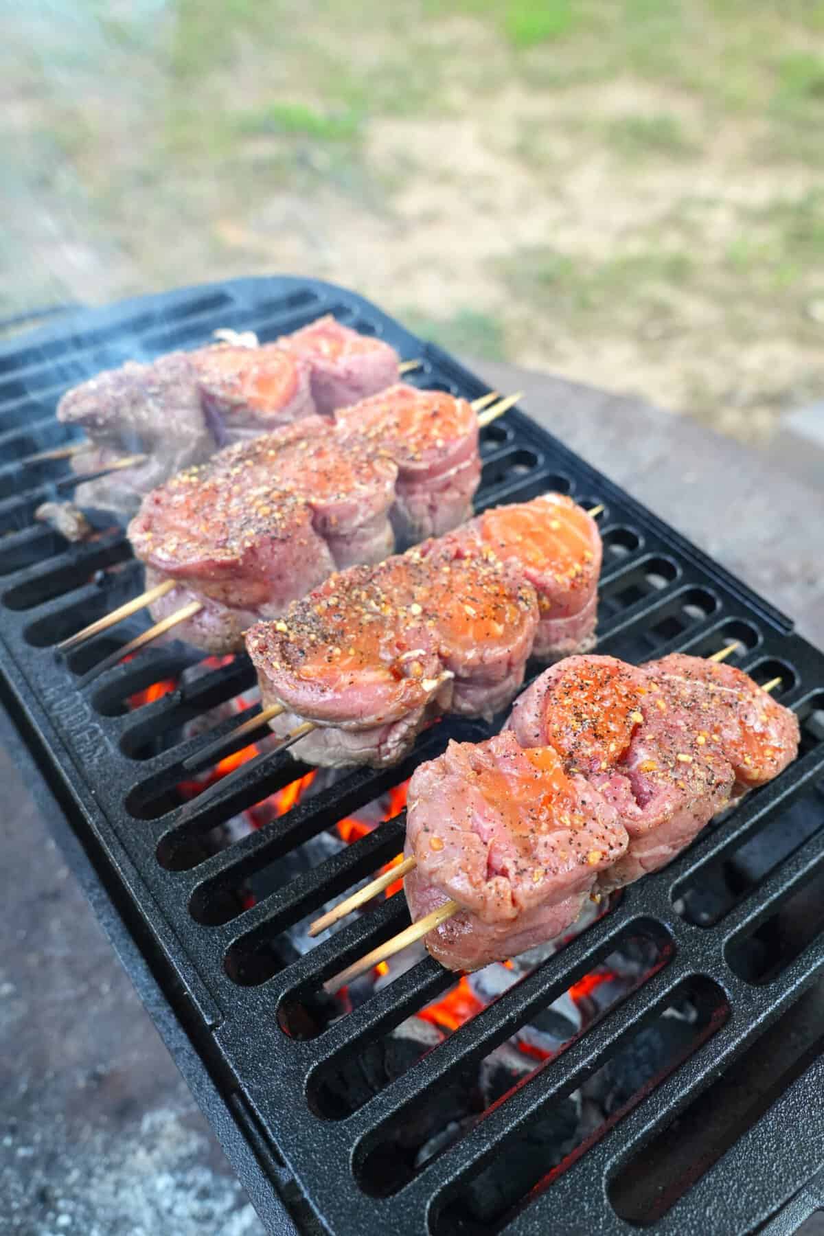 Pinwheels of beef and salmon threaded on wooden skewers and grilling on a hot grill