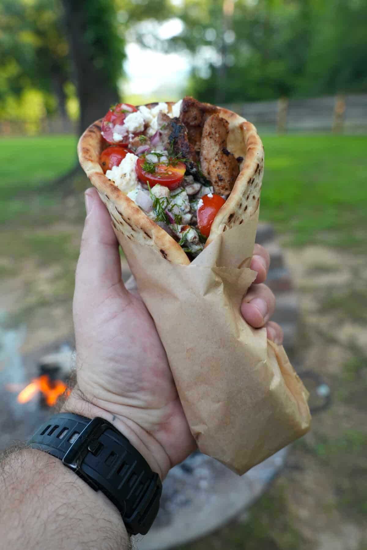 Derek Wolf holding a wrapped chicken gyro with tomatoes, tzatziki, feta and chicken visible from the top of the pita