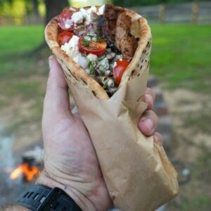 Derek Wolf holding a wrapped chicken gyro with tomatoes, tzatziki, feta and chicken visible from the top of the pita