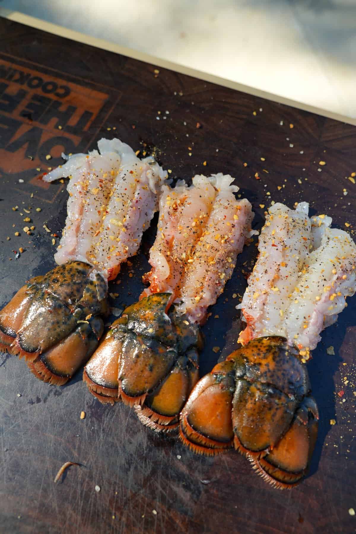 Three lobsters tails in a line on a cutting board, split open to reveal the meat