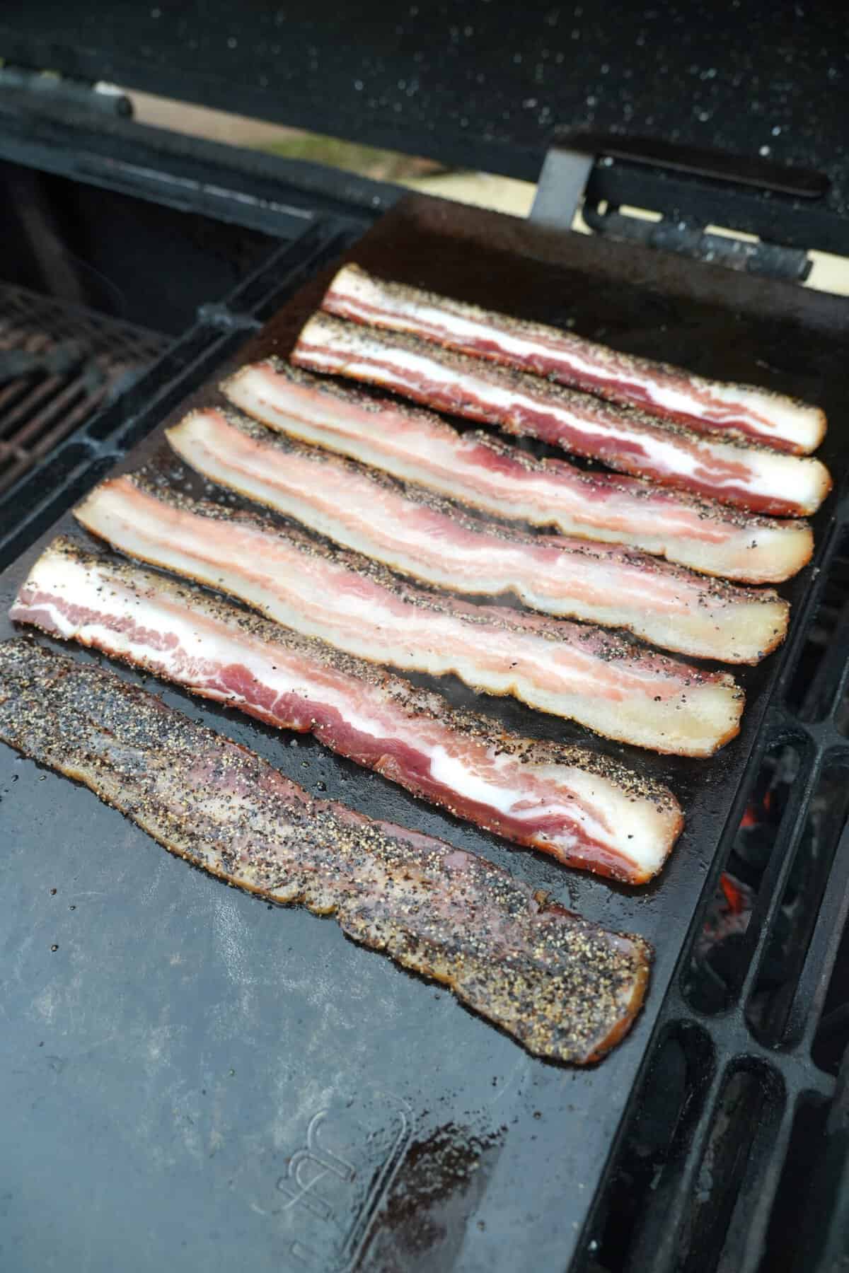 The bacon sizzles over the cast iron plancha placed over the grill.
