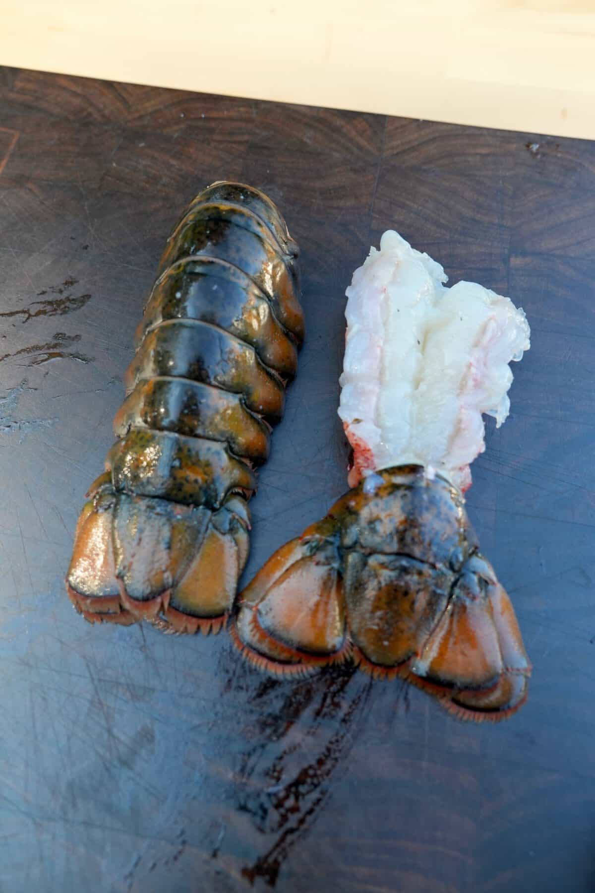 Two uncooked lobster tails, with the one on the left shell side up and the one on the right shell side down to expose the lobster meat