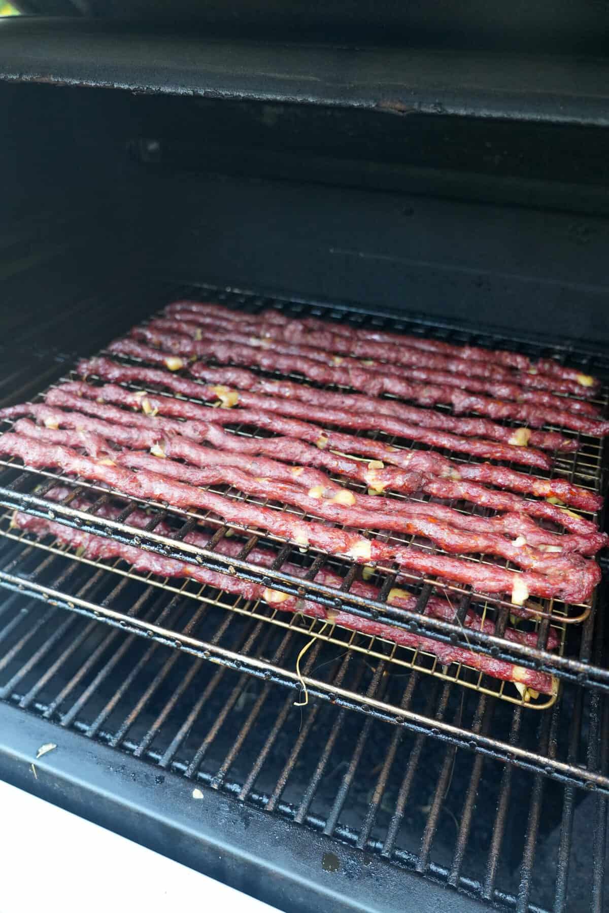 A lineup of pizza beef sticks cooking on a smoker