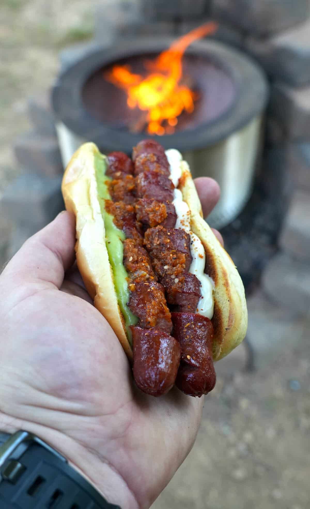 Derek Wolf holding a finished spiral hot dog in a bun with guacamole, mayonnaise, mustard and pico de gallo