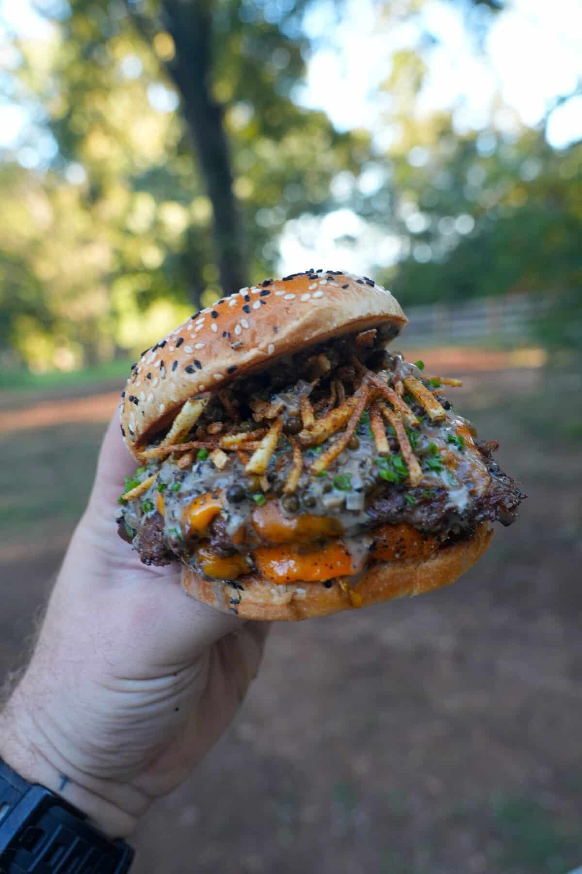 Derek Wolf holding up a finished steak au poivre burger with shoestring fries, whisky peppercorn sauce and a toasted bun