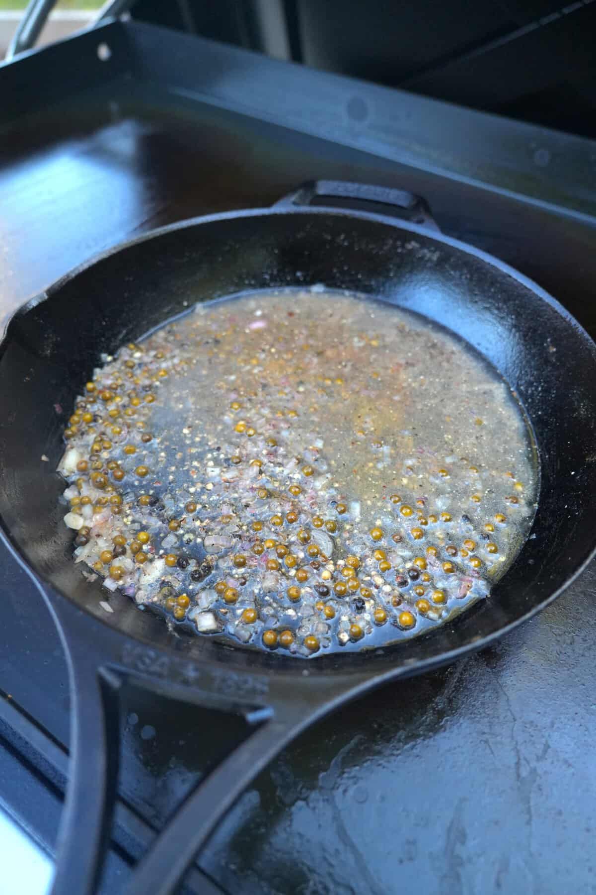 The beginning stages of a whisky peppercorn sauce, with shallots sauteeing in a cast iron skillet